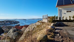 A coastal house with a solar panel roof, a stone pathway, and a view of the sea and distant buildings. - Panoramic view on Ellös top with 500m to sea | SE09125 (Ellös)