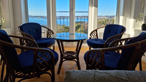 A balcony with wicker chairs and a glass table, overlooking a scenic view of the sea and hills. - Panoramic view on Ellös top with 500m to sea | SE09125 (Ellös)