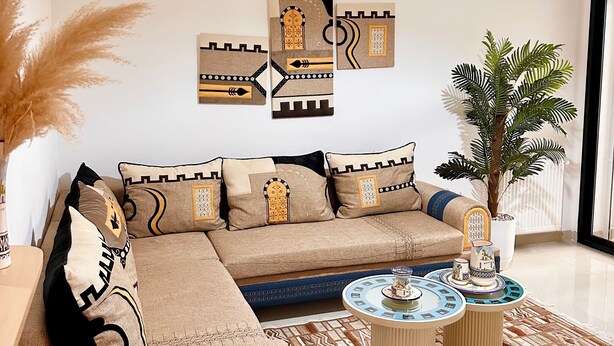Ein modernes Wohnzimmer mit einem Ecksofa, Wandbildern, einer Topfpflanze und einem runden Couchtisch.