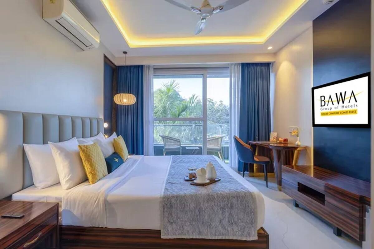 A hotel room with a bed, bedside table, desk, chair, and a view of the outdoors.