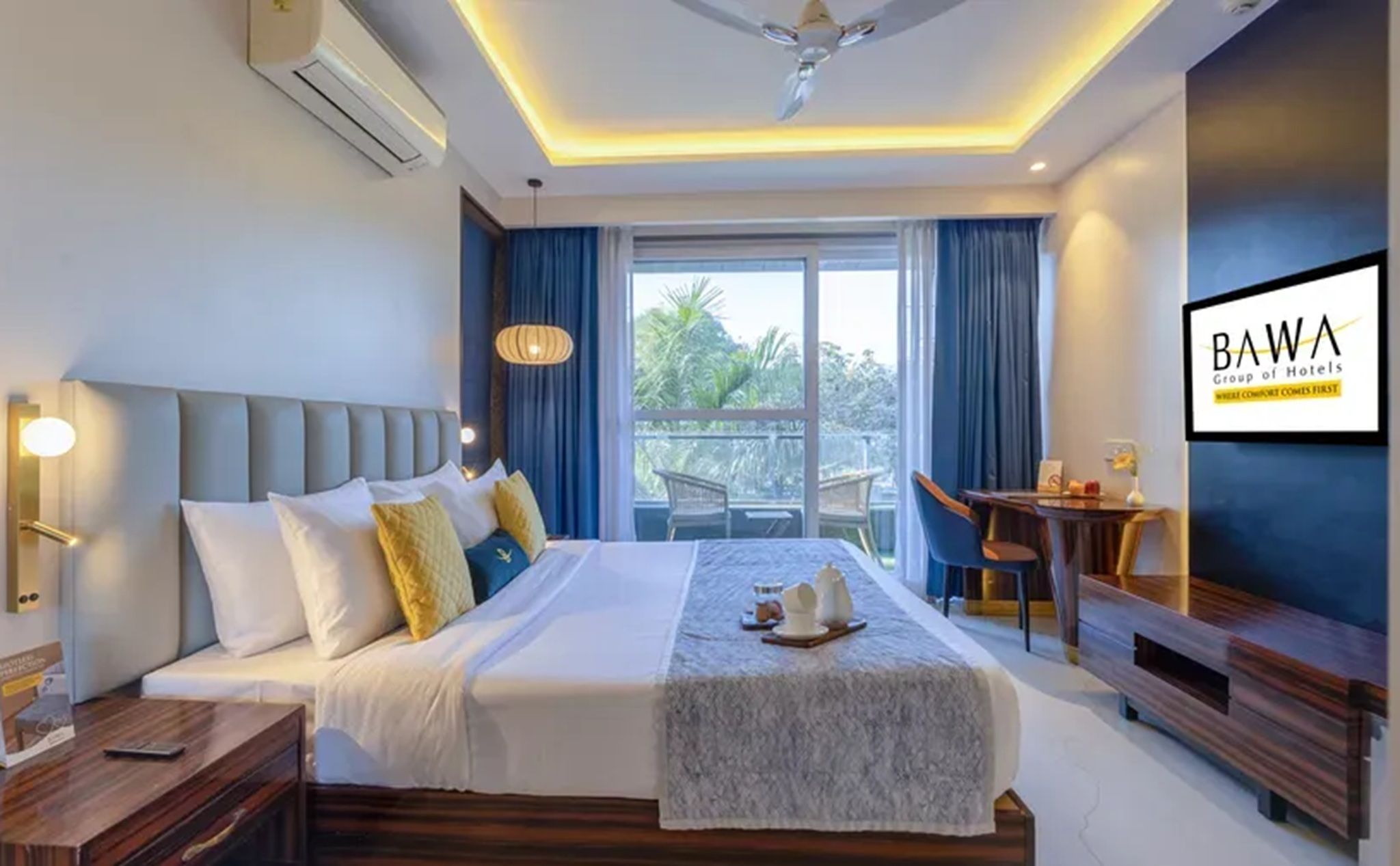 A hotel room with a bed, bedside table, desk, chair, and a view of the outdoors.