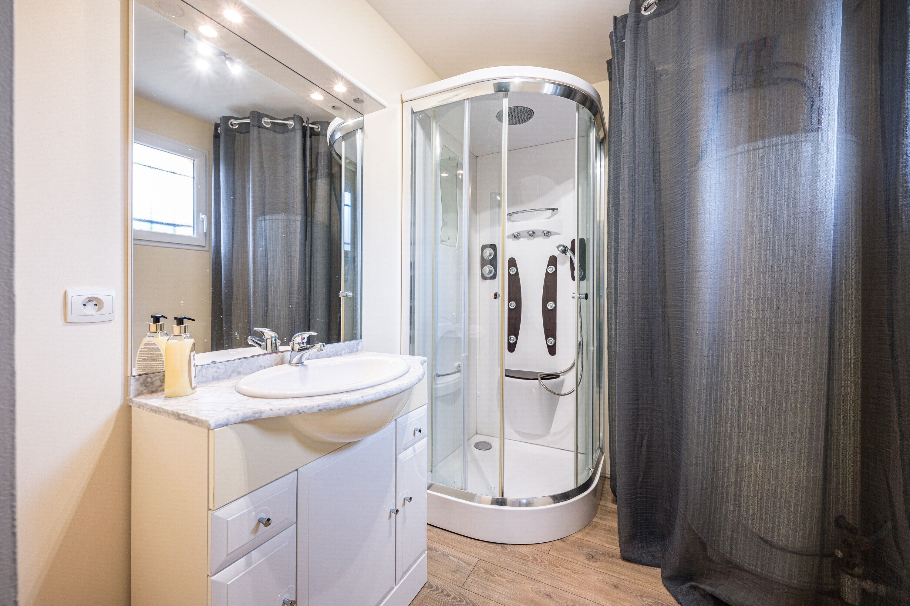 A modern bathroom with a curved shower enclosure, a sink, and a mirror.