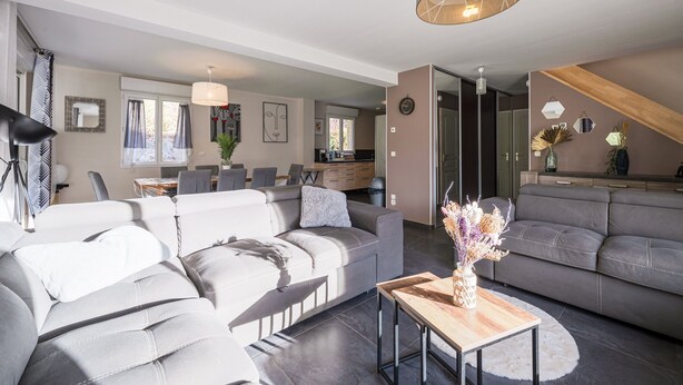 Un salon moderne avec un canapé gris, une table basse en bois et, au fond, un coin repas.
