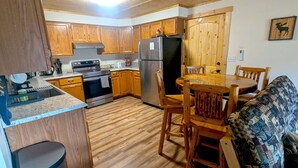 Cocina compacta con armarios de madera, refrigerador de acero inoxidable y comedor con mesa y sillas de madera.