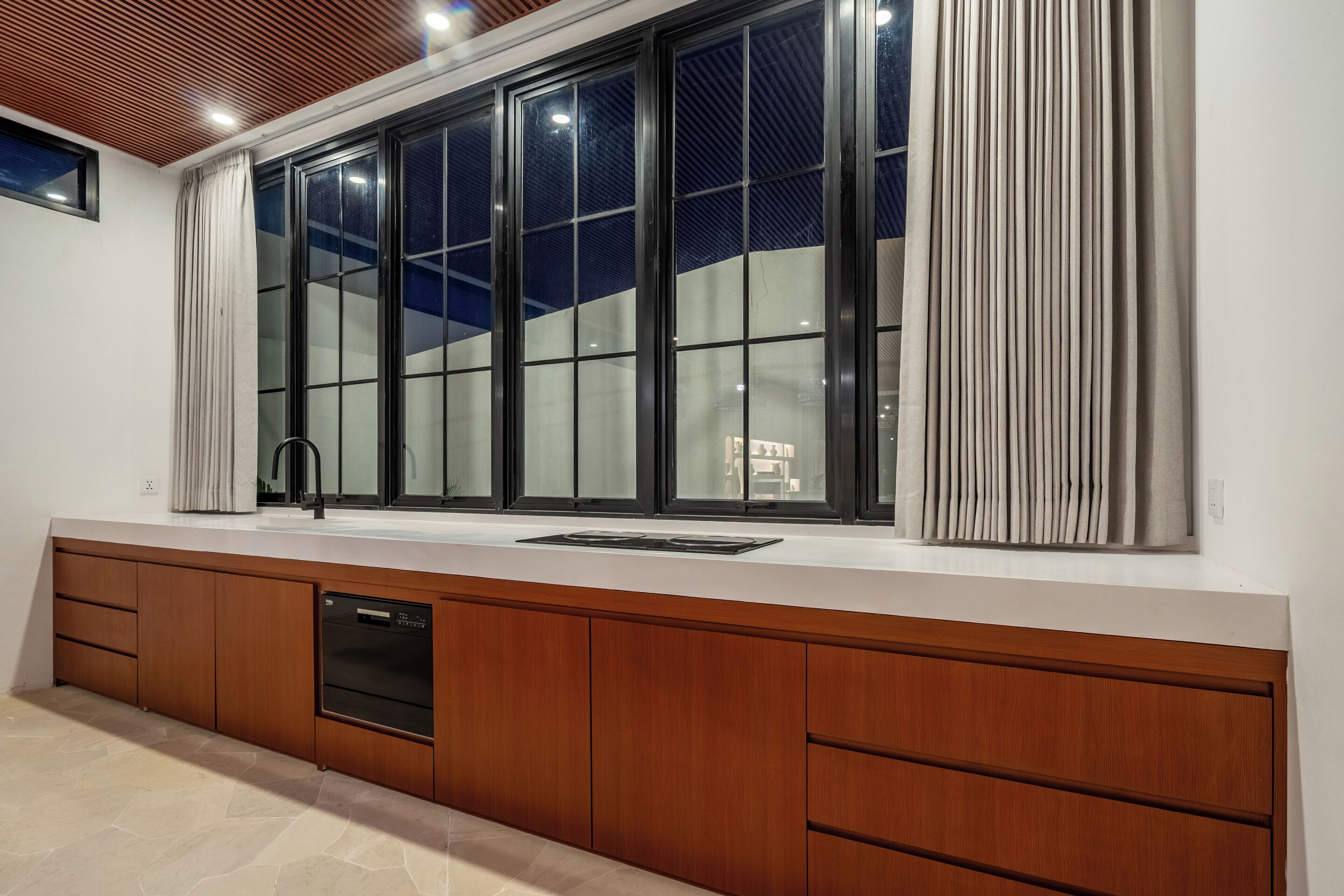 A modern kitchen with a large window, wooden cabinets, and a built-in dishwasher.