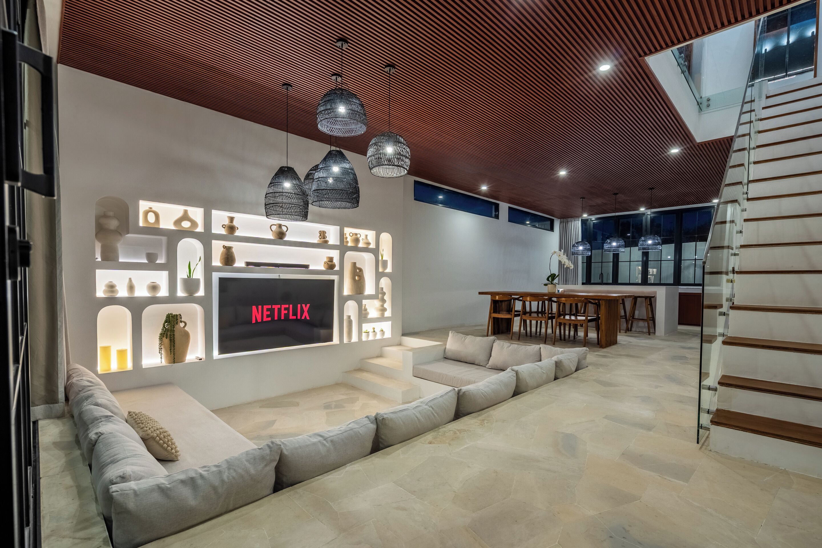 A modern living room with a sectional sofa, a flat-screen TV, and a staircase leading to an upper level.