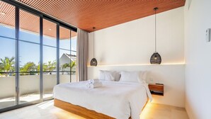 A modern bedroom with a large bed, a wooden headboard, and a view of the outdoors through floor-to-ceiling windows. - Villa Nuusa Bingin (Pecatu)