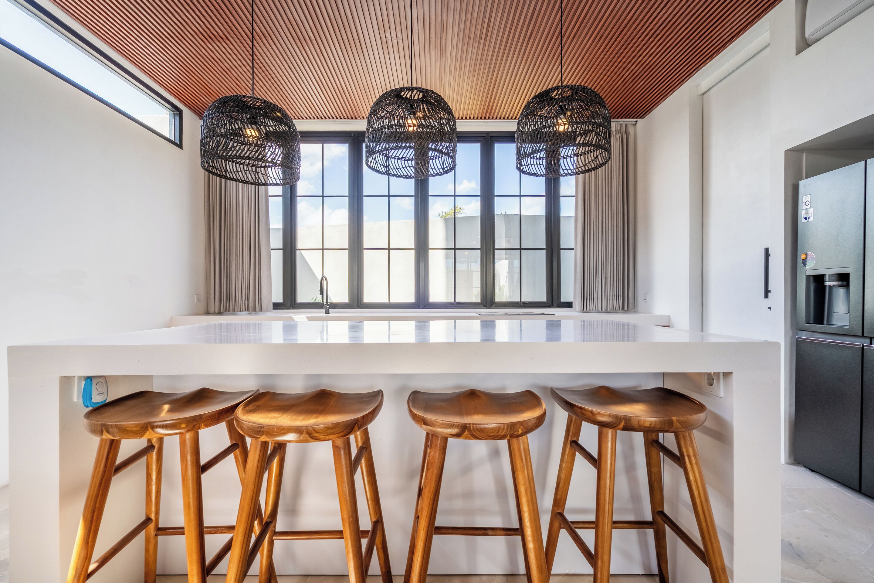 A modern kitchen with a white countertop, wooden stools, and black hanging lights.