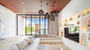 A modern living room with a large sofa, a TV, and a dining area. - Villa Nuusa Bingin (Pecatu)