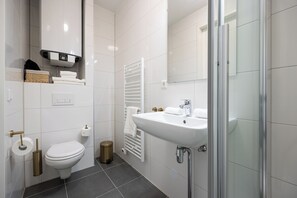 A modern bathroom with a toilet, bidet, sink, and glass shower enclosure. - Duke Studio Hotel ('s-Hertogenbosch)