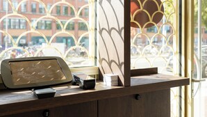 A wooden reception desk with a tablet, a cash register, and a stack of cards. - Duke Studio Hotel ('s-Hertogenbosch)