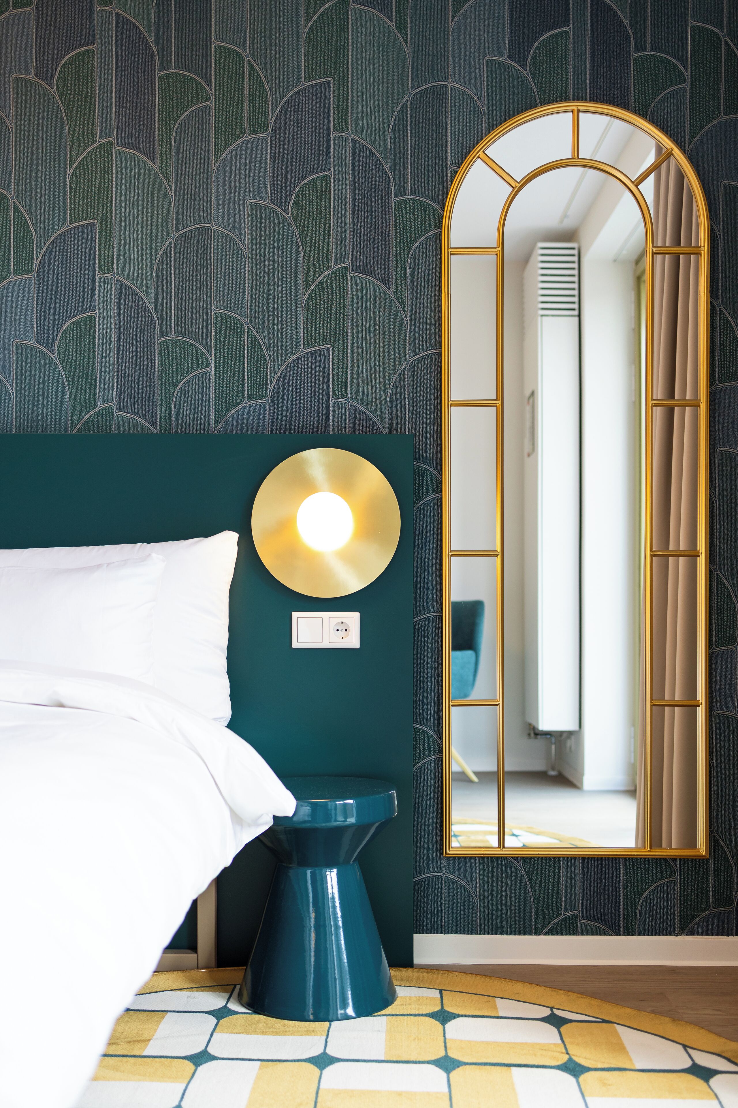 Habitación de hotel con una cama, un inodoro azul, un espejo instalado en la pared y un papel tapiz estampado.