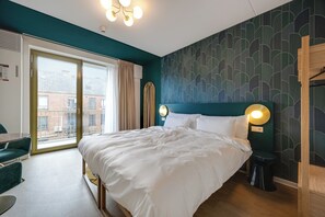 A hotel room with a large bed, a desk, and a view of the city through a large window. - Duke Studio Hotel ('s-Hertogenbosch)