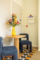 Una habitación con una mesa de madera, dos sillas azules, un jarrón amarillo con flores y una alfombra estampada.