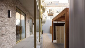 A narrow corridor with a brick wall on one side, a glass door entrance, and a wooden structure on the other. - Duke Studio Hotel ('s-Hertogenbosch)