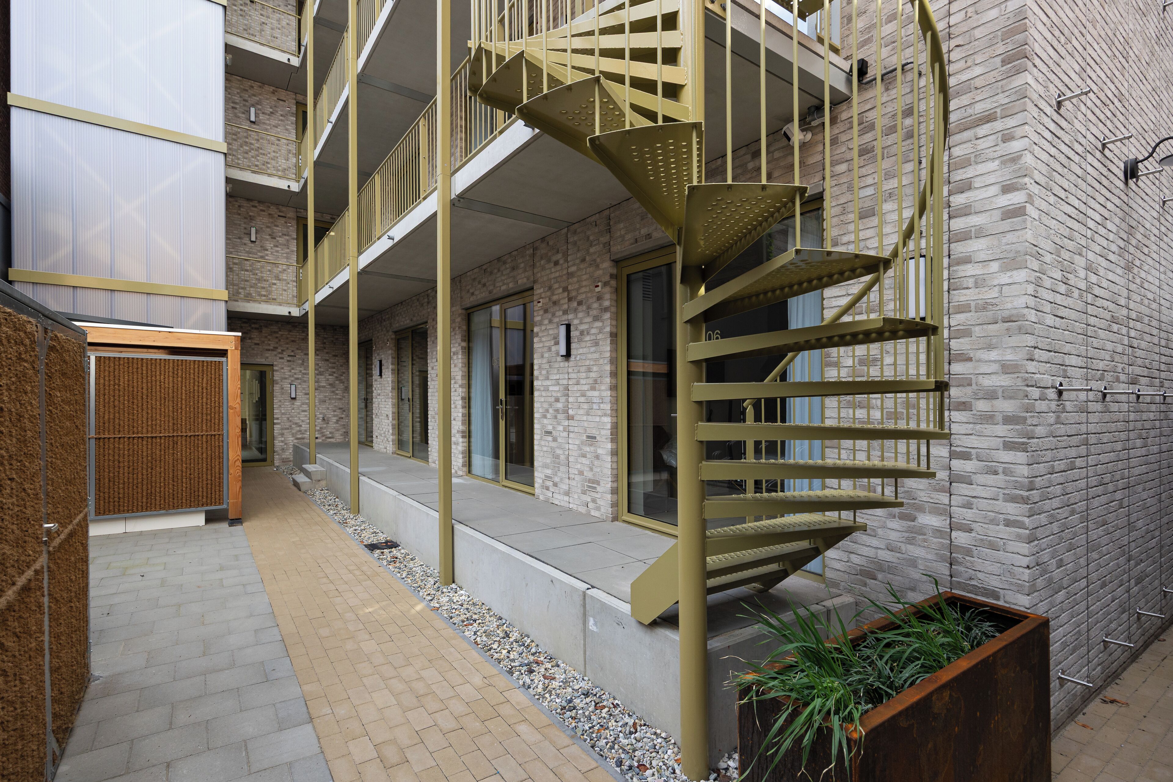 Un bâtiment moderne doté d’un escalier en colimaçon, d’une façade en briques et d’un petit jardin.