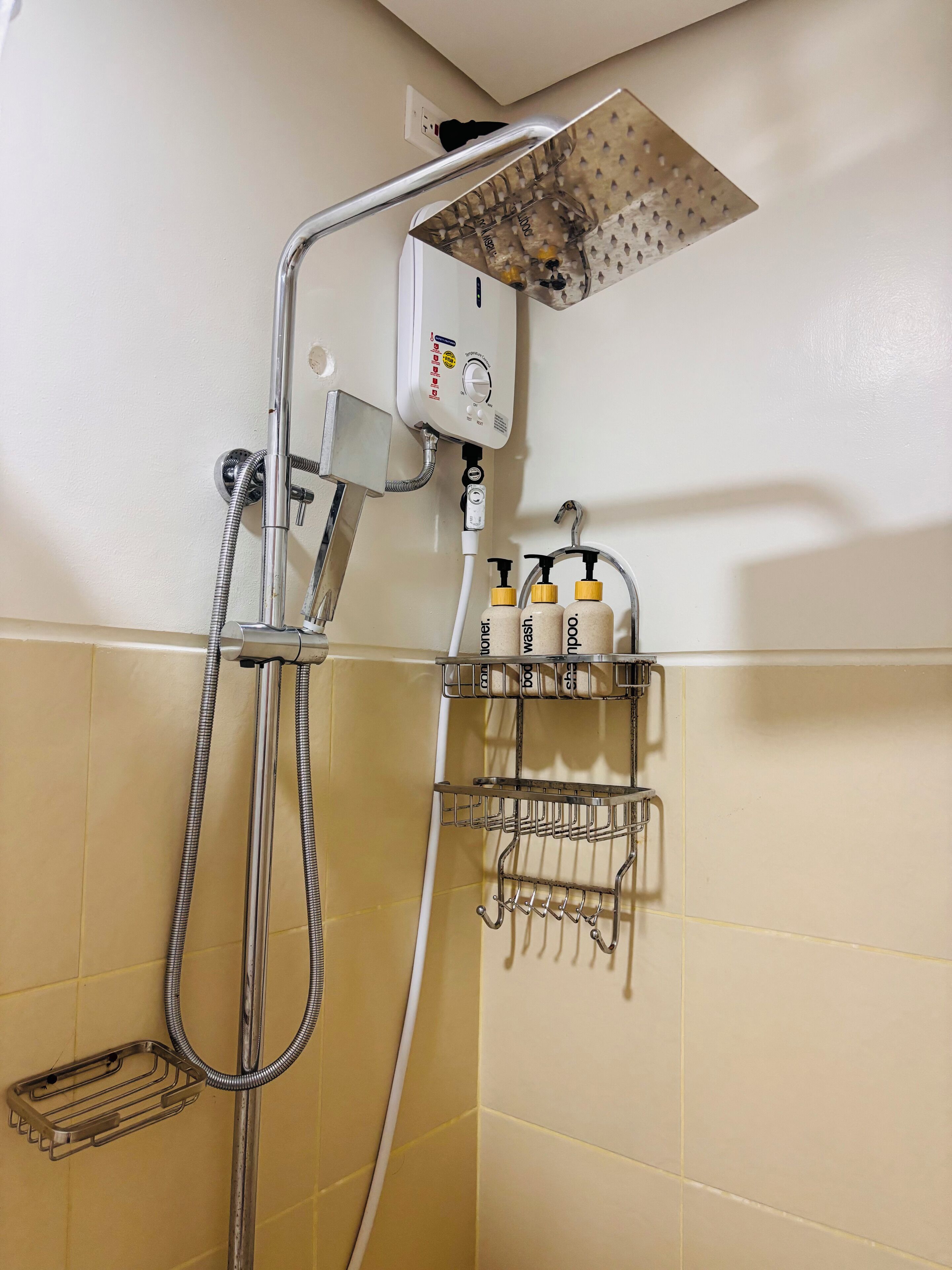 Un angolo doccia con soffione a mano, pannello di controllo a parete e ripiano con articoli da toilette.