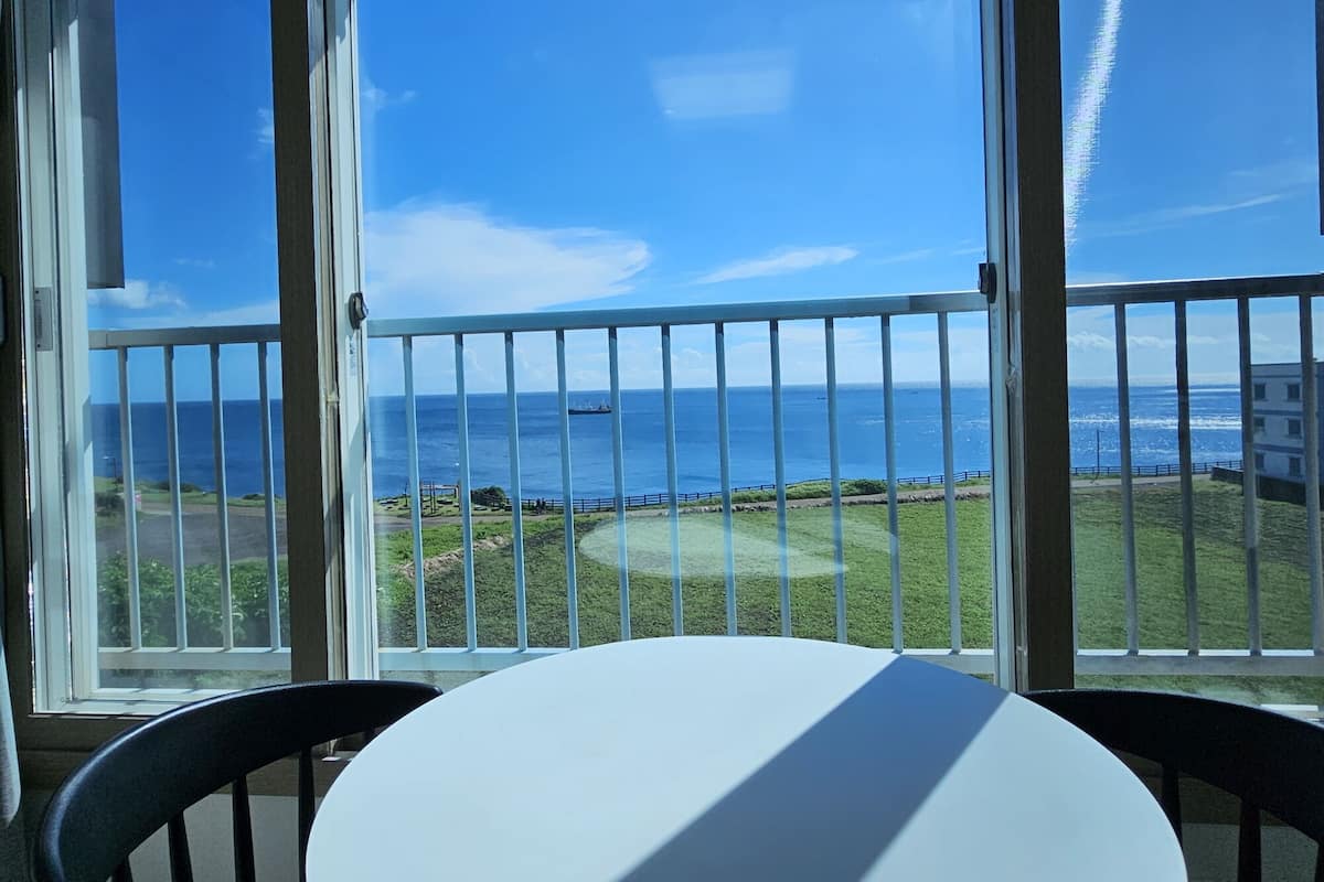 Un balcon avec vue sur l’océan, une table blanche et des chaises noires.