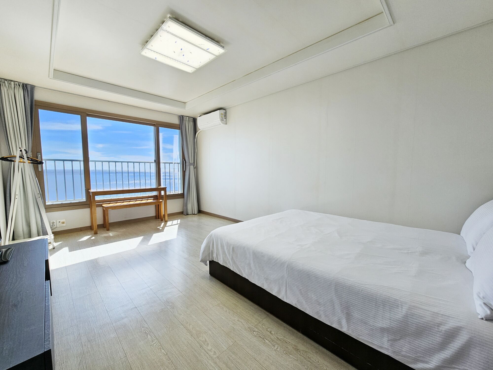 Quarto de hotel com uma cama grande, um banco junto à janela e vista para o mar.