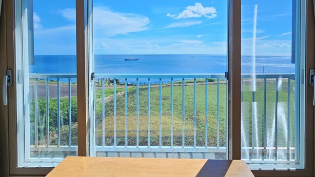 Quarto com uma grande janela com vista para a costa, incluindo o oceano e um navio.