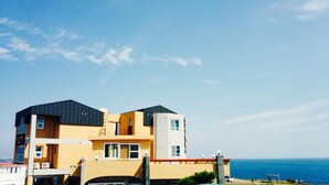 Um edifício moderno de vários andares com telhado plano, janelas amplas e vista para o oceano.