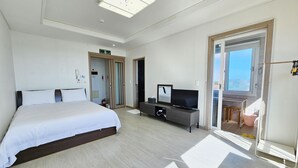 Quarto de hotel com uma cama grande, televisão, escrivaninha e vista da cidade por uma porta de varanda.