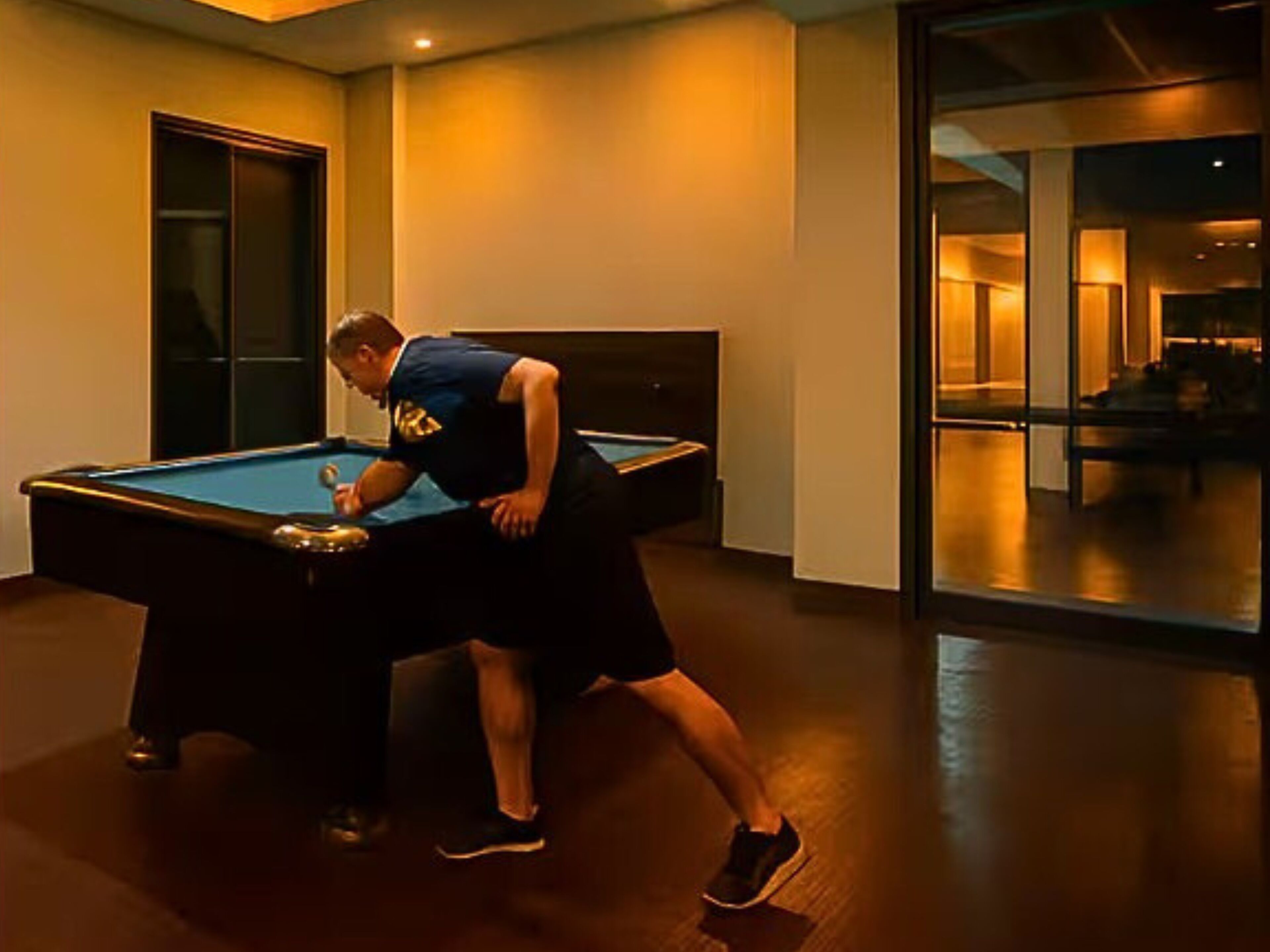 A pool table in a room with a glass door leading to another area.