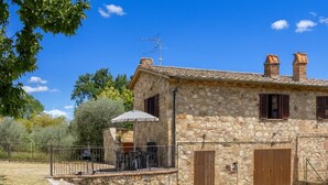 Una casa de piedra con un patio, una zona de estar cubierta al aire libre y un jardín vallado.