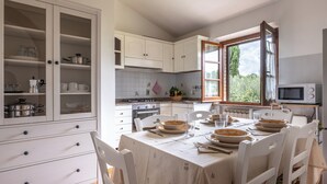 Una cocina con armarios blancos, una mesa de comedor preparada para cuatro personas y una ventana con vistas a la vegetación.