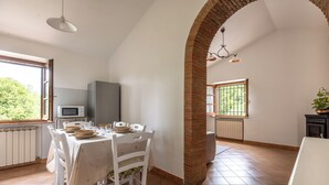Un comedor con un arco de ladrillo, sillas blancas, una mesa dispuesta para dos personas y vistas al exterior.
