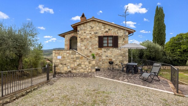 Un edificio de piedra con un pequeño patio, mobiliario exterior y vistas del paisaje circundante.
