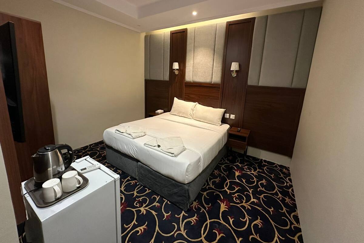 A hotel room with a bed, bedside lamps, a coffee maker, and a tray with cups and a kettle.