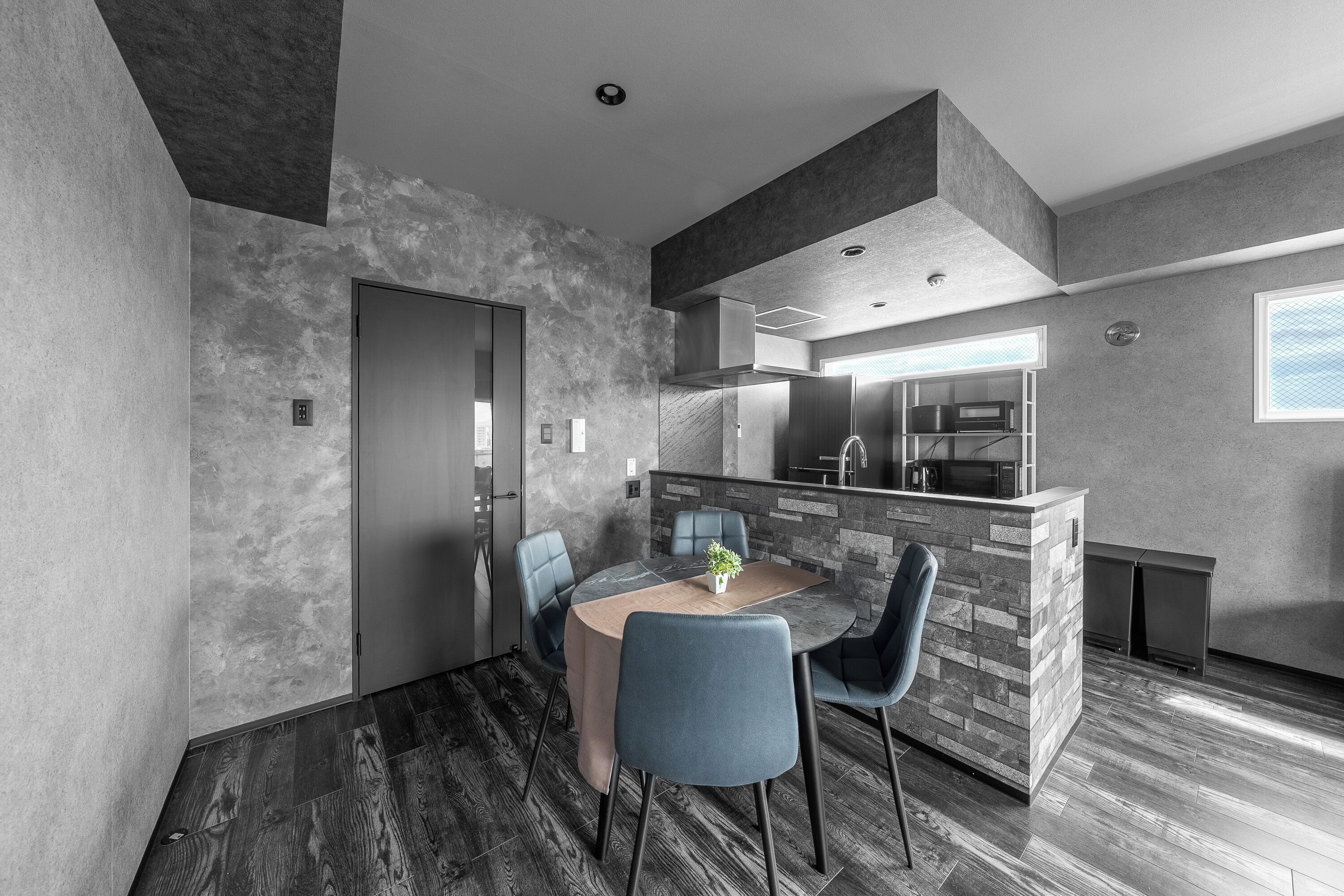 A modern kitchen with a central island, a dining area with a round table and chairs, and a visible door leading to another room.