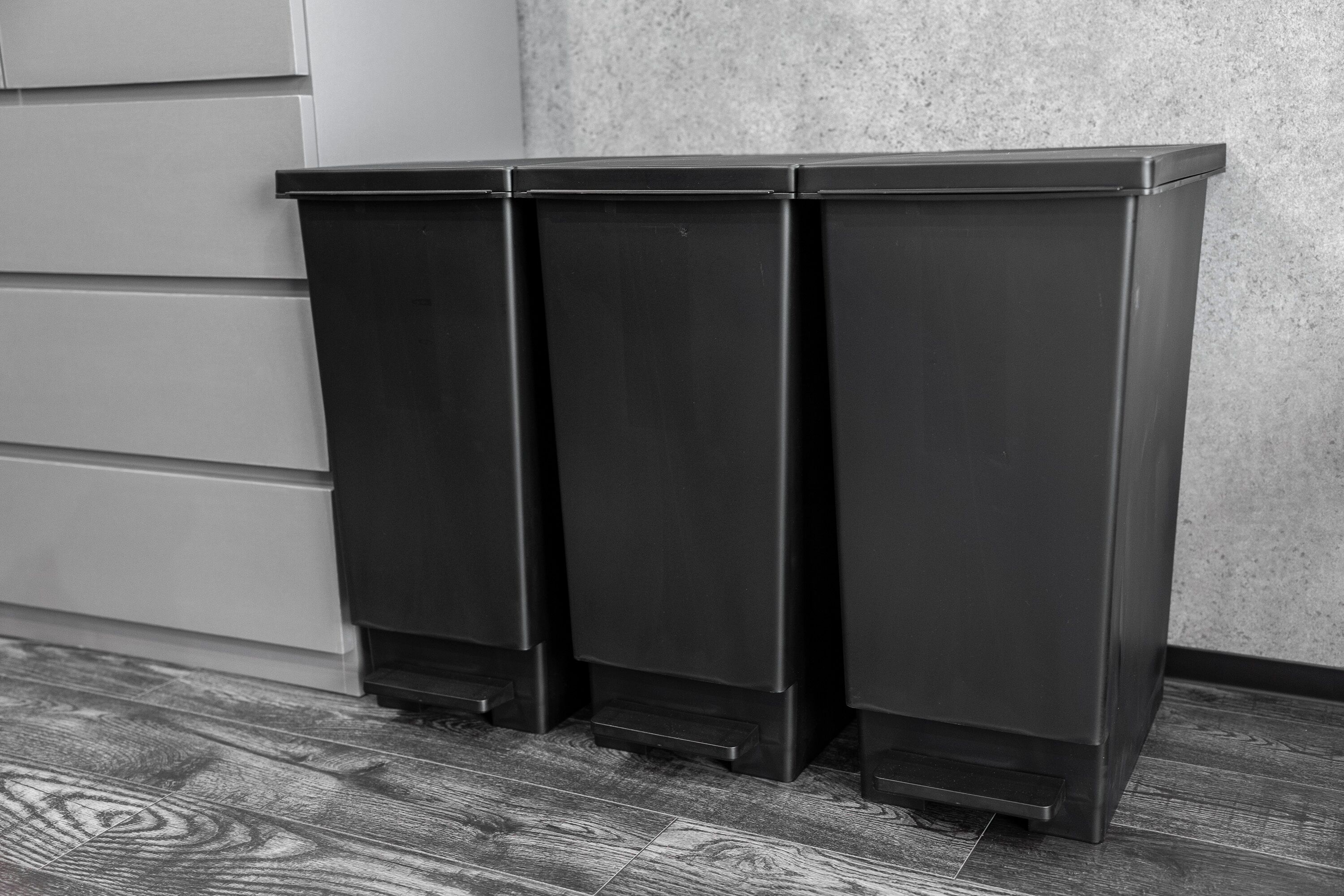 Three black trash bins against a wall with a textured surface.