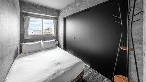 A modern bedroom with a large bed, a wardrobe, and a view of the city through a window. - J-STAR 901 (Sapporo)