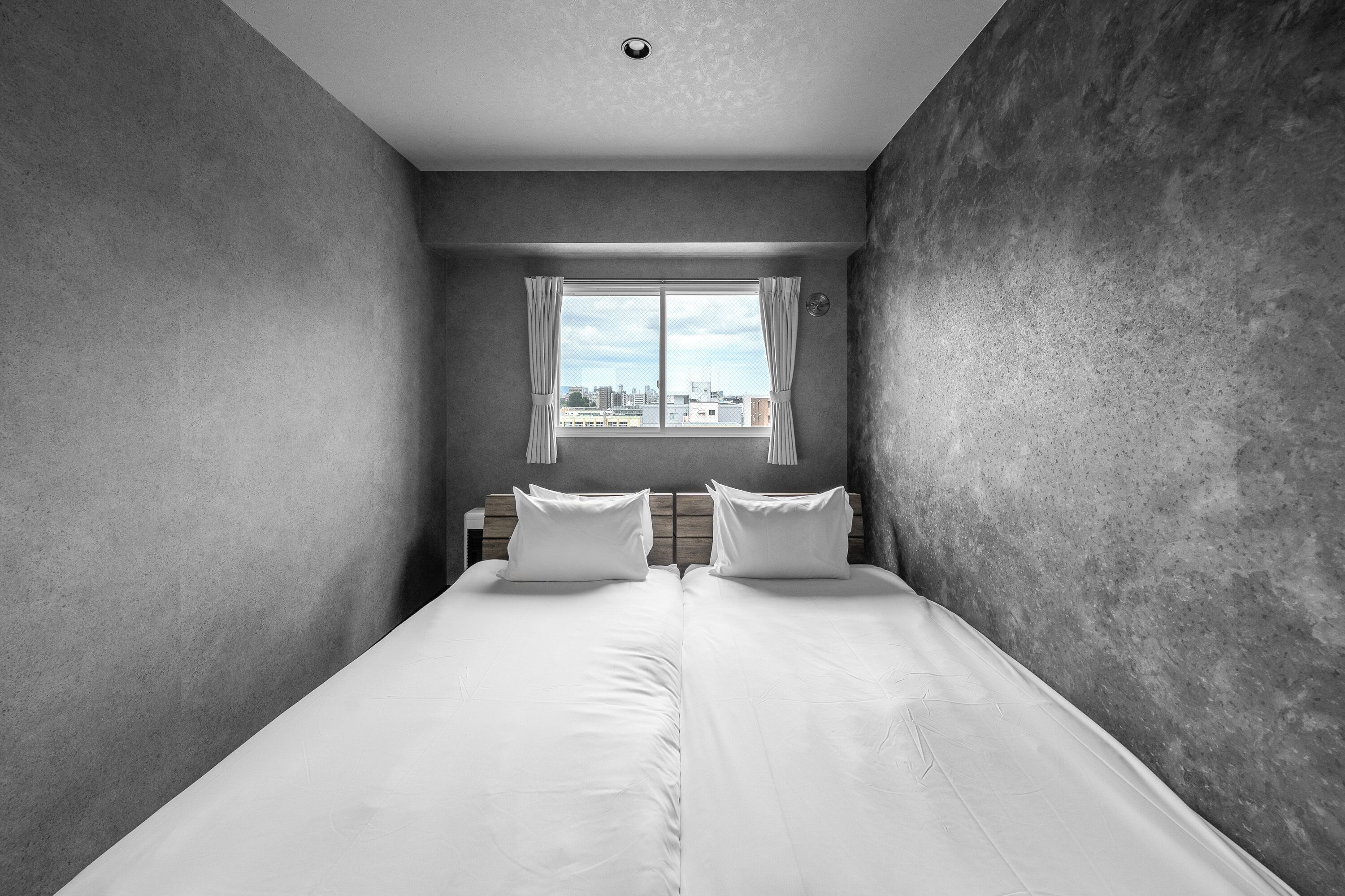 A narrow, modern bedroom with a large window, a wooden headboard, and a city view.