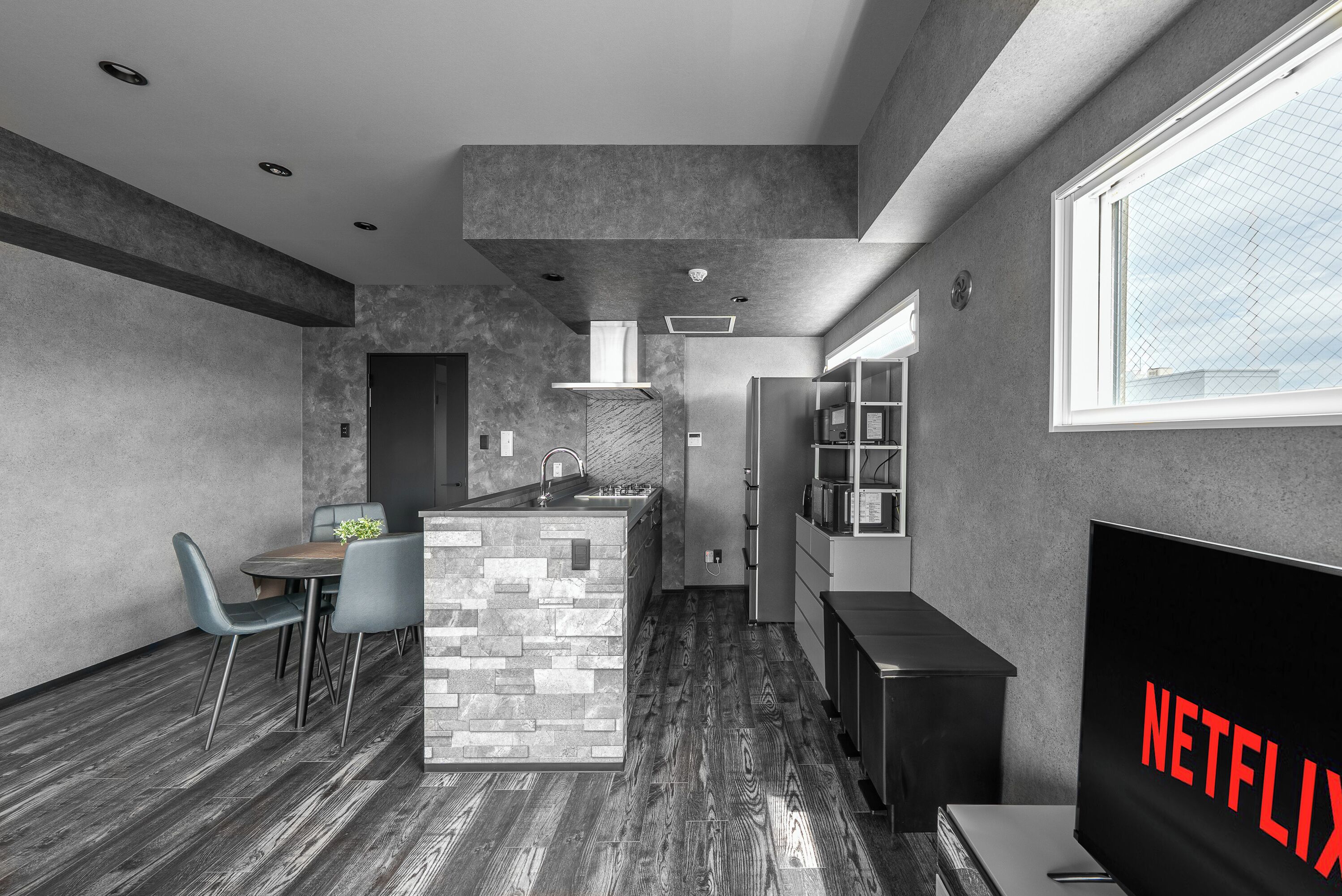 A modern kitchen with a stone island, a dining area with chairs, a built-in TV, and a large window.