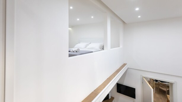 Ein modernes Hotelzimmer mit einem großen Bett, einem kleinen Fenster und Blick auf das Nachbarzimmer.