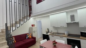 Eine moderne Küche mit weißen Schränken, einem Esstisch mit Stühlen, einem roten Sofa und einer Treppe mit schwarzen Geländern.