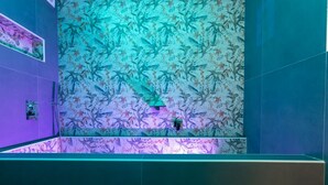 Ein Badezimmer mit floralem Wandpapier, einem Spiegel und violettem Licht.
