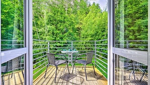 Una terraza de madera con una mesa y sillas, rodeada de paredes de vidrio que dan a un follaje verde y tupido.