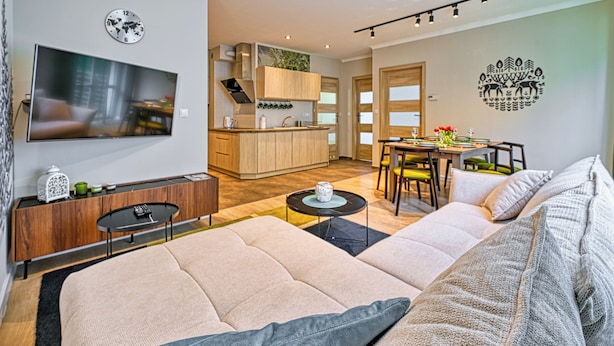 Una sala moderna con un sofá, un televisor, un comedor con mesa y sillas, y una cocina al fondo.