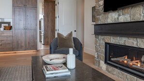 A living room with a stone fireplace, a television mounted on the wall, and a wooden cabinet.