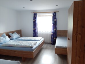 A bedroom with two wooden beds, a window with curtains, and a wooden wardrobe.