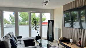 A modern living room with a grey sectional sofa, a glass coffee table, a potted plant, a large mirror, and a wooden console table with decorative items.