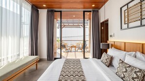 Hotelkamer met een groot bed, een bankje, uitzicht op het balkon en een houten plafond.
