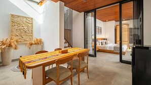 Een moderne hotelkamer met een houten eettafel, stoelen en een bed met een geborduurd beddegoed.