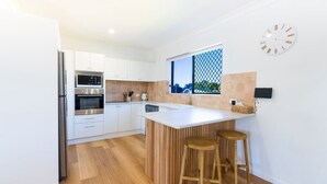 A modern kitchen with white cabinets, stainless steel appliances, a large island with stools, and a view through a window.