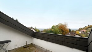 A balcony with a view of houses and trees, a small table, and a satellite dish.