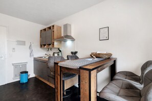 Eine kleine Küche mit integriertem Herd, einem Holzschrank und einer blauen Mülltonne.